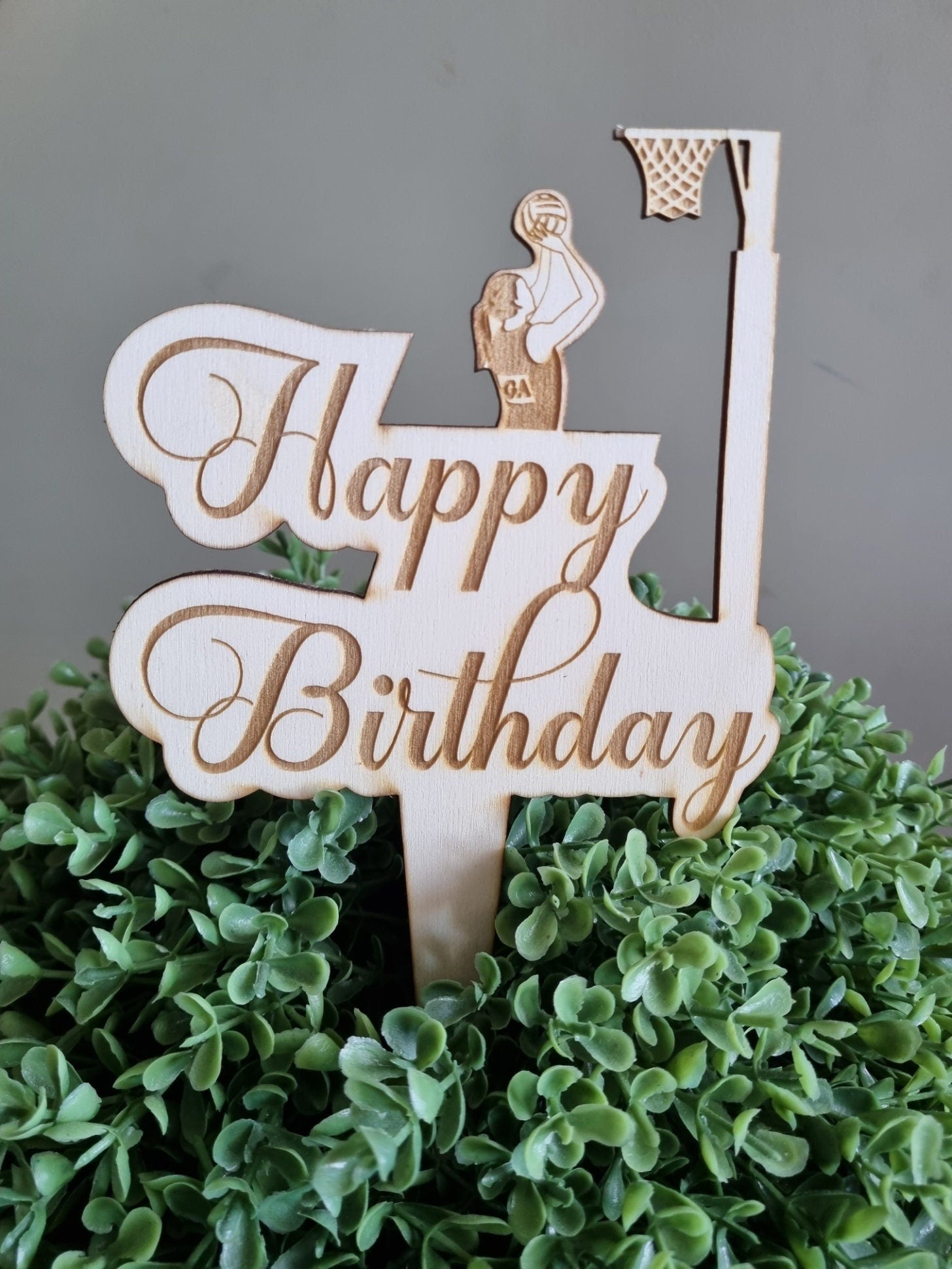 Wooden Cake Topper engraved with the words Happy Birthday. Featuring a girl shooting a goal into a netball ring