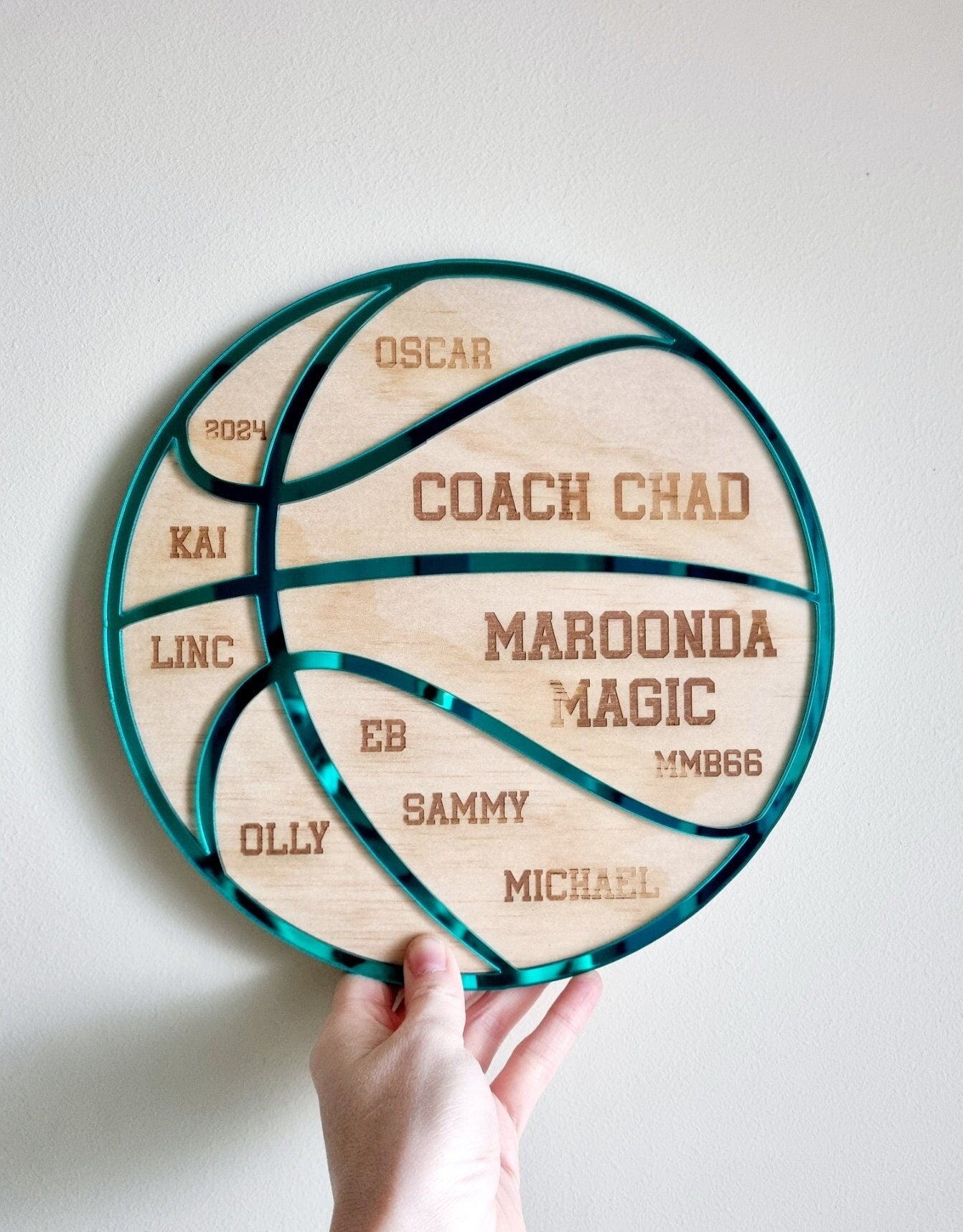 Personalised basketball coach gift set displayed on a white surface. The custom wooden plaque is shaped like a basketball with engraved team names, player numbers, and the coach’s name, accented with a green mirrored acrylic overlay