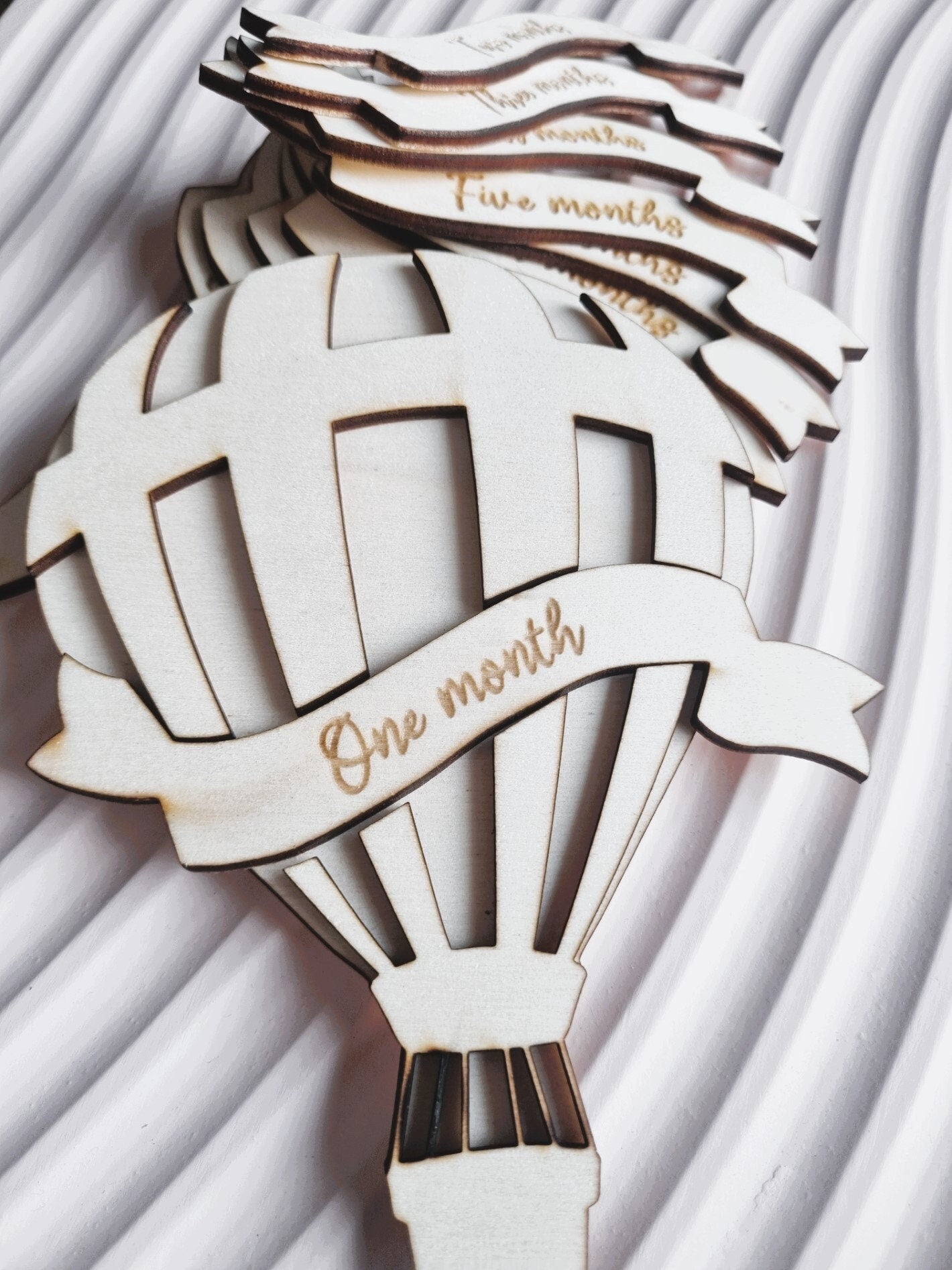 Baby Milestone photo prop set. The main piece is cut in the shape of a hot air balloon and each monthly milestone is engraved on a ribbon shaped piece of wood  that is interchangeable  in the centre of the balloon.