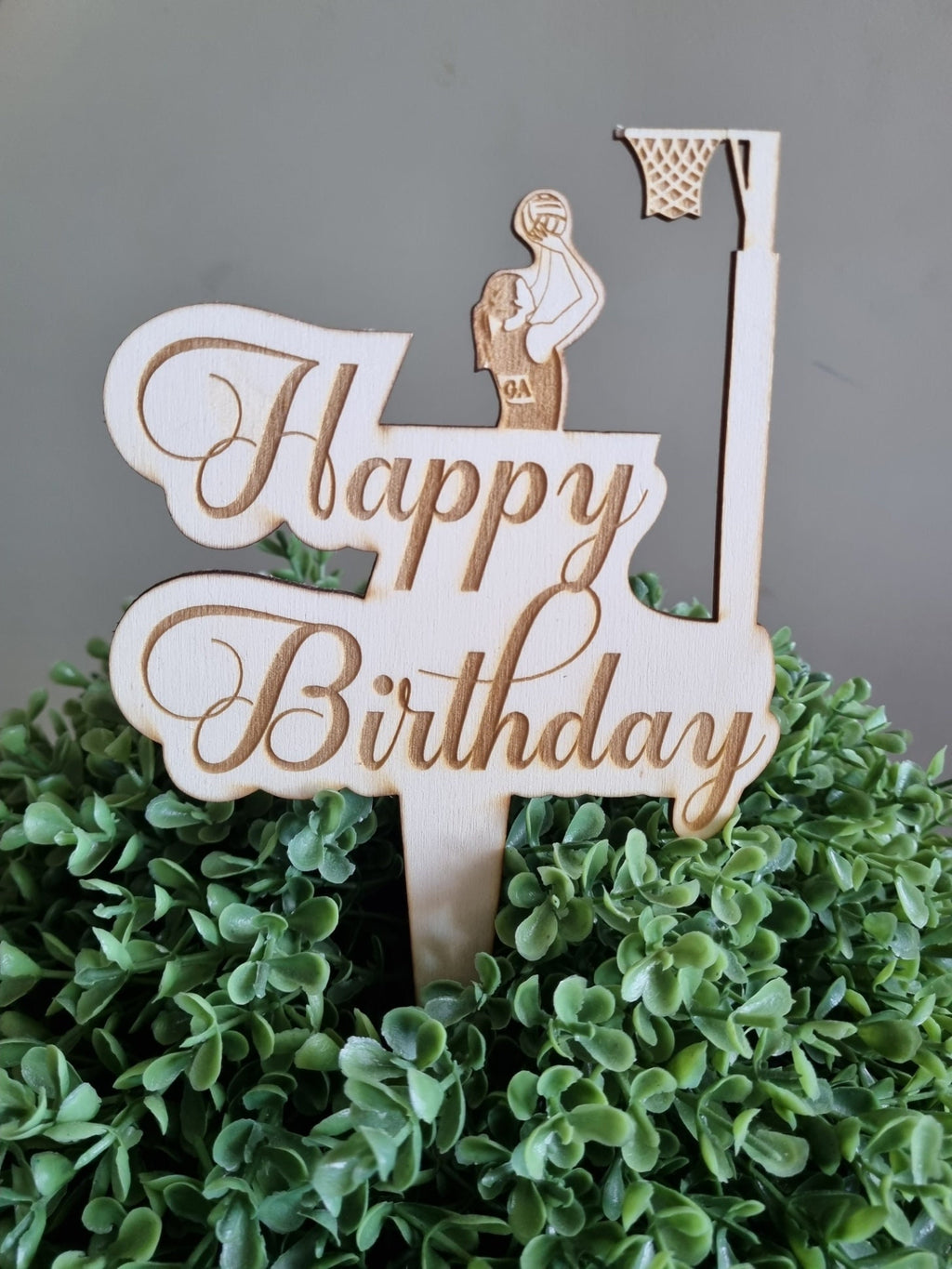 Wooden Cake Topper engraved with the words Happy Birthday. Featuring a girl shooting a goal into a netball ring